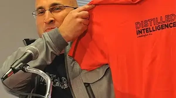 Man at a microphone holding a Distilled Intelligence shirt